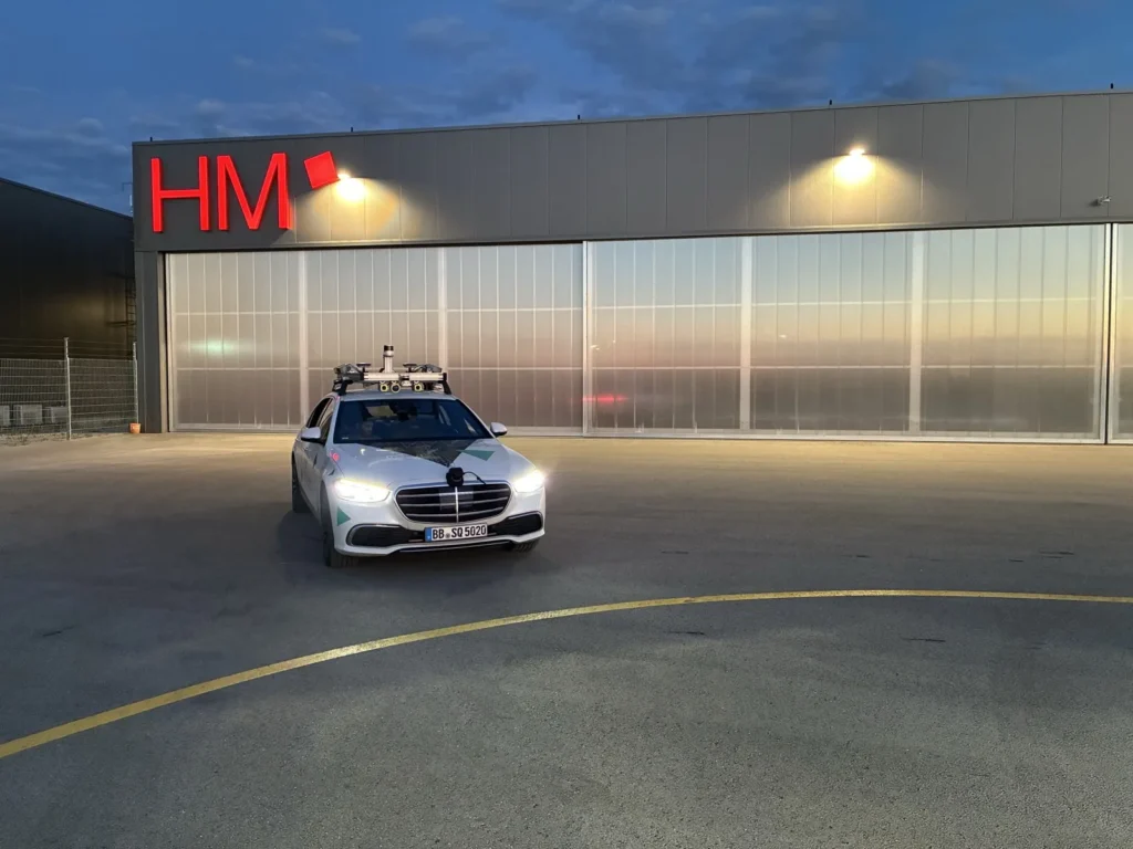 The test vehicle in front of the lit hangar at dusk